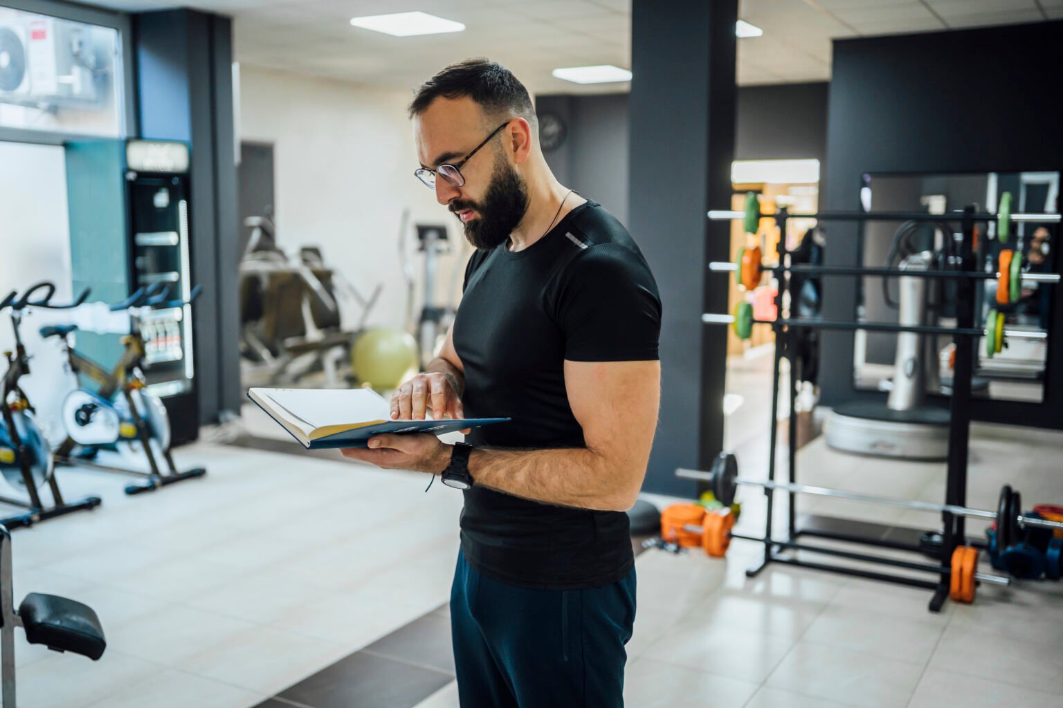 Young male fitness trainer standing in the gym and reading exercise schedule