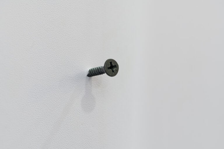 A screw inserted into a piece of drywall.